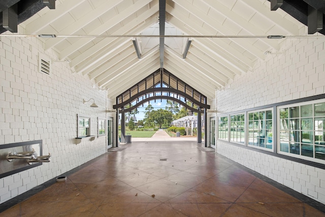 hallway featuring high vaulted ceiling, brick wall, and beam ceiling