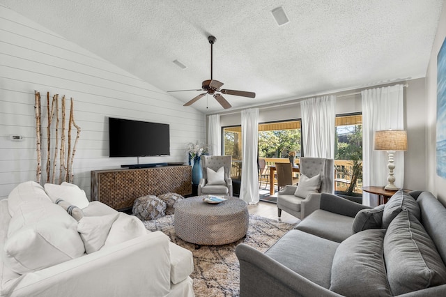 living room with lofted ceiling, hardwood / wood-style floors, ceiling fan, a textured ceiling, and wood walls