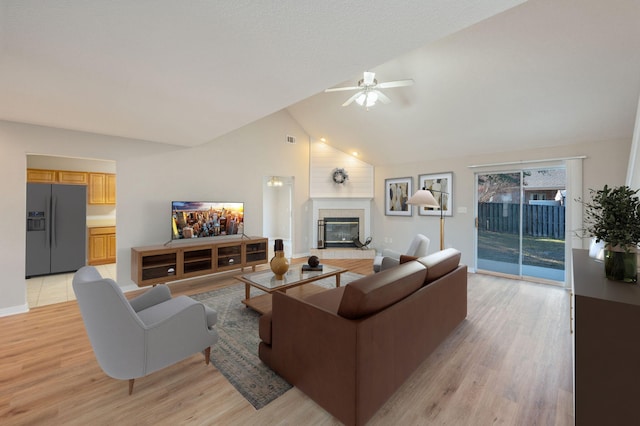 living room with ceiling fan, light wood-type flooring, high vaulted ceiling, and a tiled fireplace