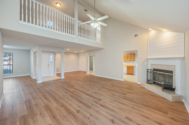 unfurnished living room featuring ceiling fan, a tile fireplace, high vaulted ceiling, and light hardwood / wood-style flooring