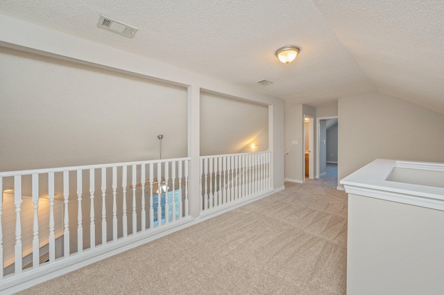 hallway with a textured ceiling, carpet floors, and vaulted ceiling