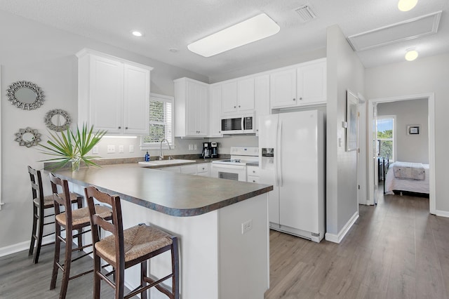 kitchen featuring white appliances, a healthy amount of sunlight, white cabinetry, and kitchen peninsula