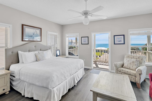 bedroom featuring a textured ceiling, dark hardwood / wood-style flooring, access to exterior, ceiling fan, and a water view