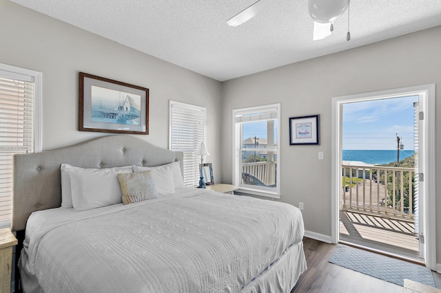 bedroom with access to outside, wood-type flooring, a water view, a textured ceiling, and ceiling fan