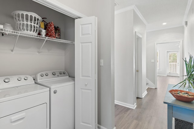 clothes washing area with ornamental molding, washing machine and dryer, and light wood-type flooring