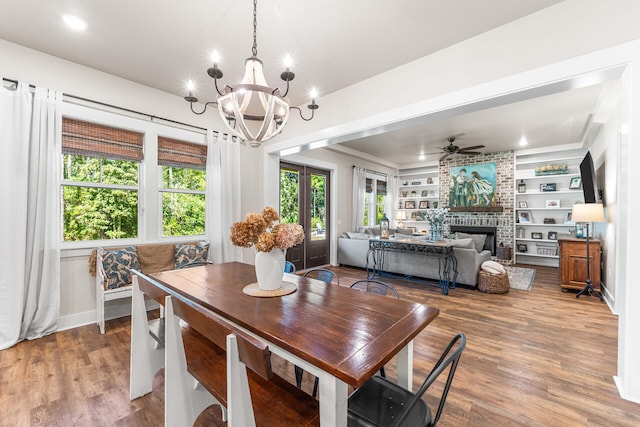 dining room featuring ceiling fan with notable chandelier, built in features, wood-type flooring, and a fireplace