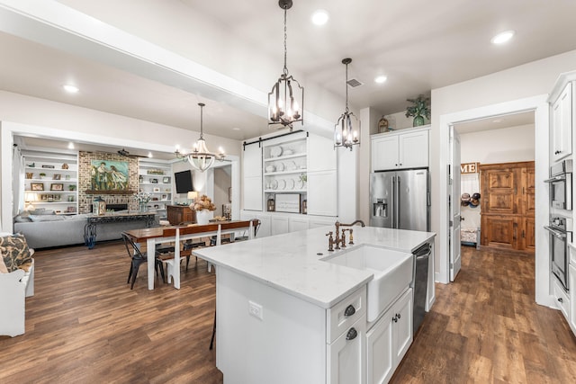 kitchen with white cabinetry, stainless steel appliances, decorative light fixtures, dark wood-type flooring, and a center island with sink