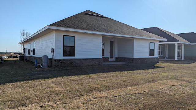 rear view of house with central AC and a lawn