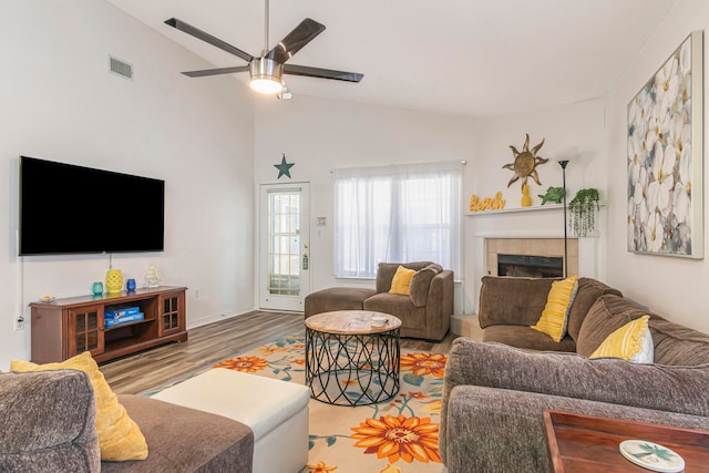 living room featuring high vaulted ceiling, hardwood / wood-style flooring, a tile fireplace, and ceiling fan