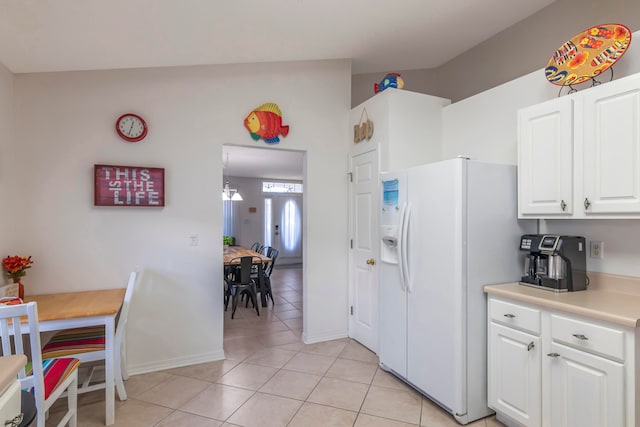 kitchen with lofted ceiling, white cabinets, light tile patterned flooring, and white refrigerator with ice dispenser