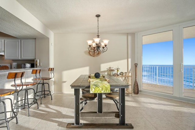 tiled dining space featuring a textured ceiling, a water view, an inviting chandelier, and expansive windows