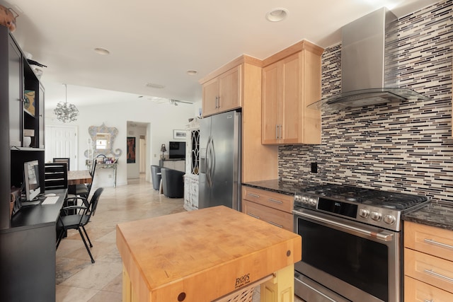 kitchen with tasteful backsplash, wall chimney range hood, stainless steel appliances, dark stone countertops, and light brown cabinets