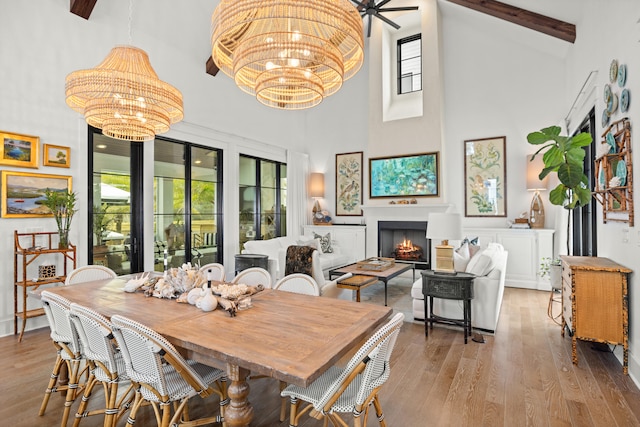 dining area with ceiling fan with notable chandelier, light hardwood / wood-style floors, beam ceiling, and high vaulted ceiling