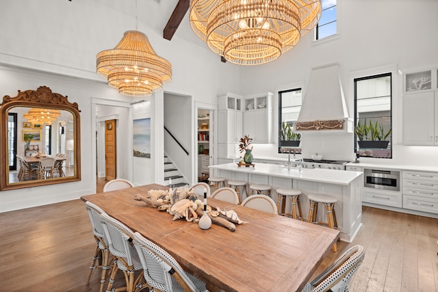 dining area with a towering ceiling, beam ceiling, light wood-type flooring, and an inviting chandelier