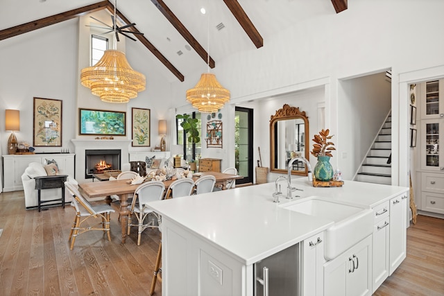 kitchen with sink, an inviting chandelier, light hardwood / wood-style flooring, high vaulted ceiling, and an island with sink