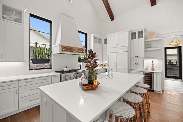 kitchen with beam ceiling, premium range hood, wine cooler, and an island with sink