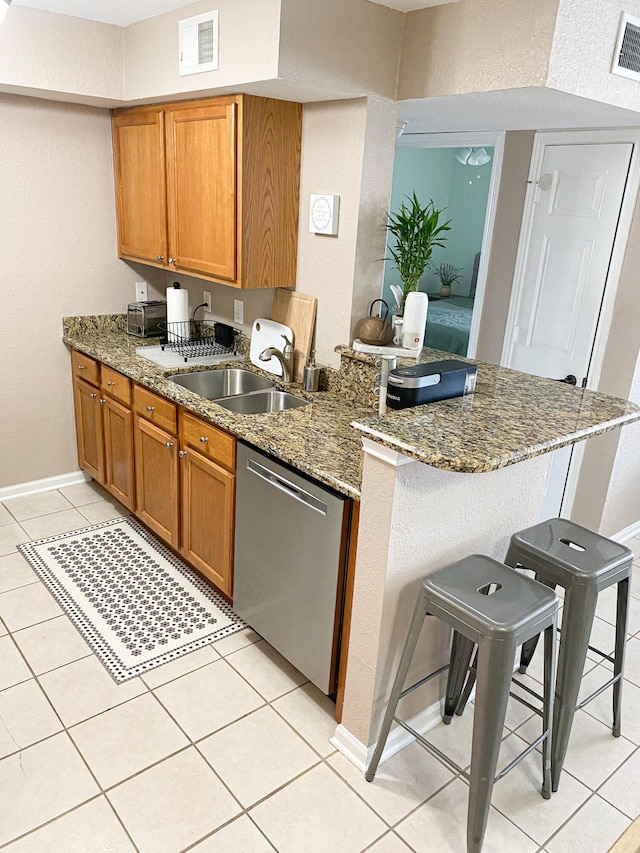 kitchen with stone countertops, a peninsula, a sink, dishwasher, and a kitchen bar