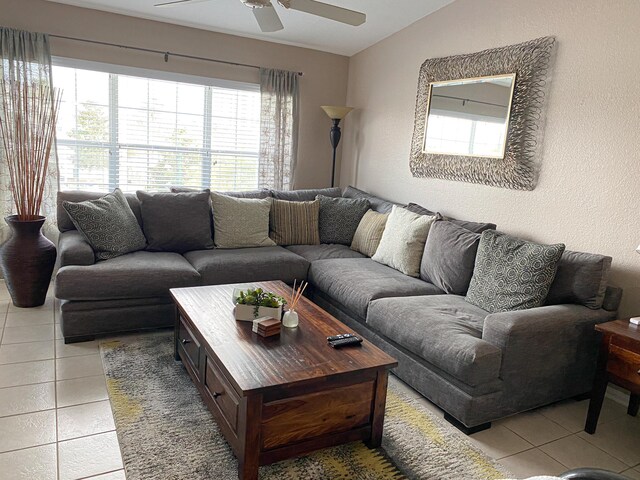 living area with lofted ceiling, a textured wall, ceiling fan, and light tile patterned flooring