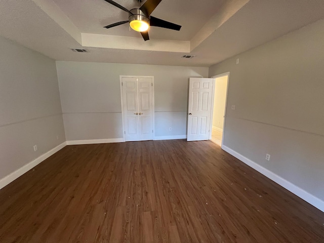 empty room featuring a ceiling fan, dark wood-style flooring, visible vents, baseboards, and a tray ceiling