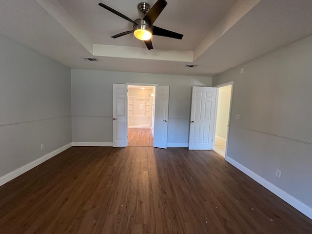 unfurnished bedroom with baseboards, visible vents, dark wood-style floors, and a raised ceiling