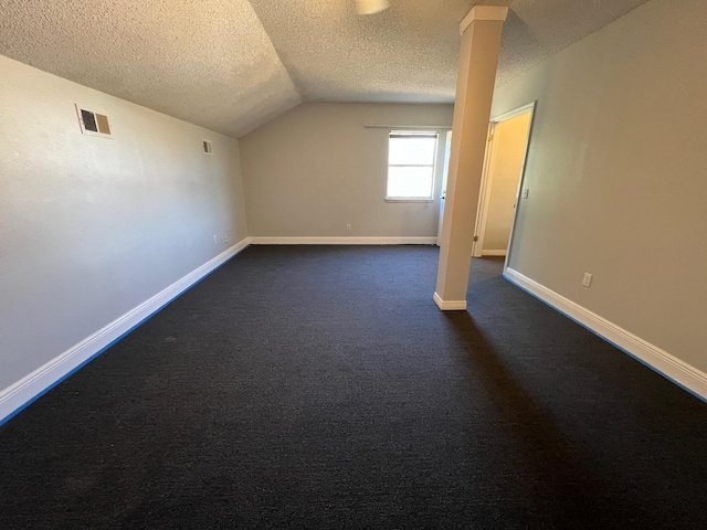 additional living space featuring visible vents, lofted ceiling, baseboards, dark colored carpet, and a textured ceiling