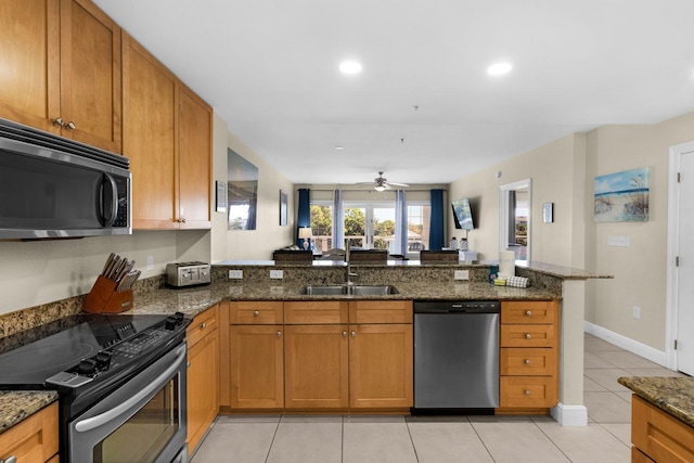 kitchen with kitchen peninsula, dark stone counters, light tile patterned flooring, sink, and stainless steel appliances