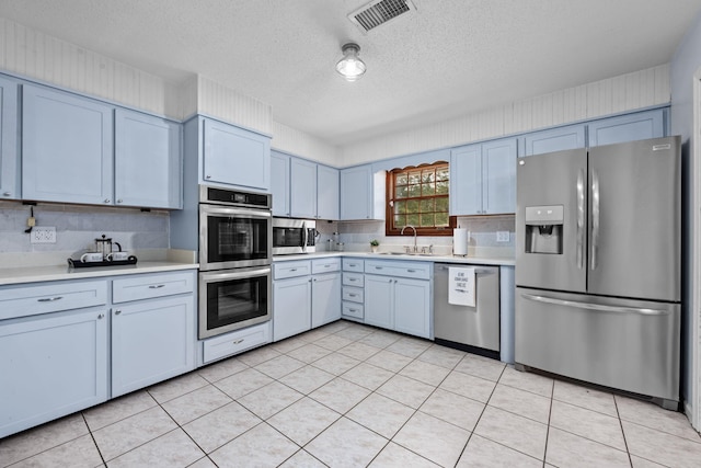 kitchen with stainless steel appliances, a sink, visible vents, light countertops, and backsplash