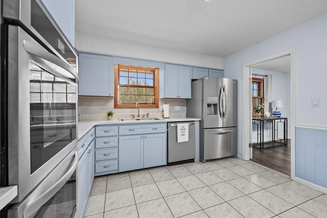 kitchen featuring light tile patterned floors, a textured ceiling, a sink, light countertops, and appliances with stainless steel finishes