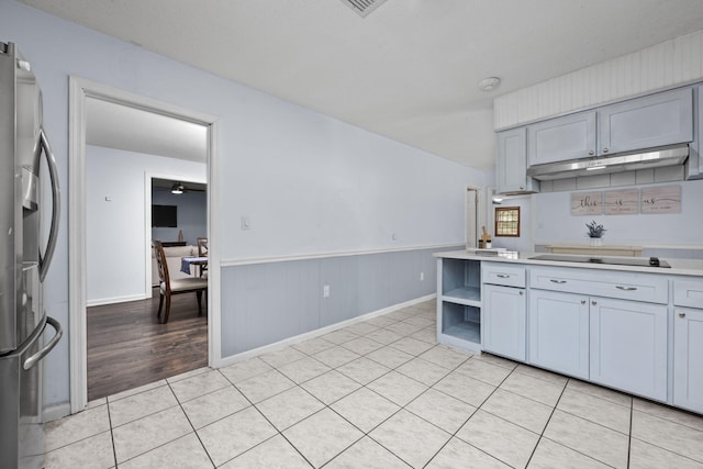 kitchen featuring stainless steel fridge, black electric stovetop, light countertops, under cabinet range hood, and open shelves