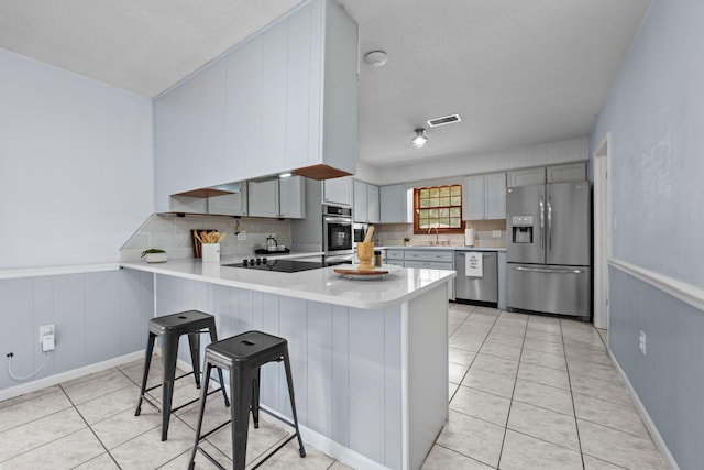 kitchen with stainless steel appliances, a peninsula, a kitchen breakfast bar, light countertops, and gray cabinets