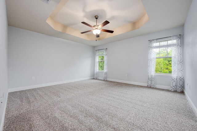 carpeted spare room with a raised ceiling and ceiling fan