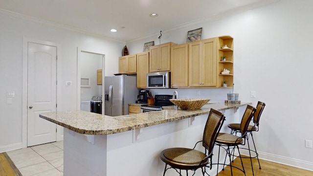 kitchen with light wood-type flooring, kitchen peninsula, stainless steel appliances, light stone counters, and a breakfast bar area