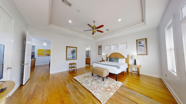 bedroom with ceiling fan, a raised ceiling, and light wood-type flooring