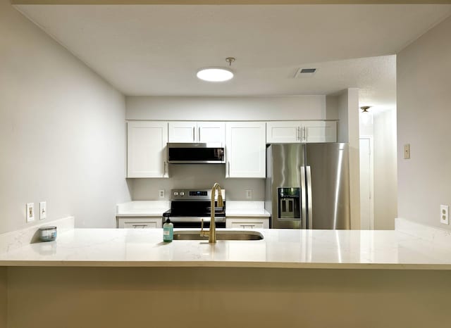 kitchen with appliances with stainless steel finishes, sink, kitchen peninsula, white cabinetry, and light stone counters