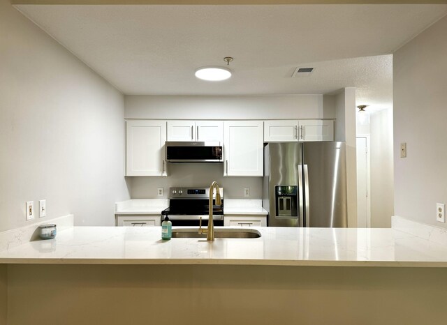 200 Sandestin Ln Unit 1307, Miramar Beach, FL 32550 - kitchen featuring appliances with stainless steel finishes, a sink, a peninsula, white cabinets, and light stone counters