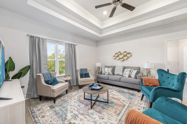 living room with ceiling fan, hardwood / wood-style flooring, ornamental molding, and a raised ceiling