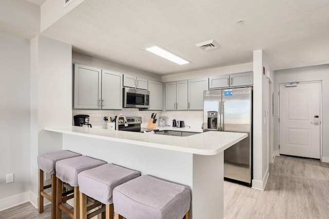 kitchen with kitchen peninsula, gray cabinetry, a breakfast bar, appliances with stainless steel finishes, and tasteful backsplash