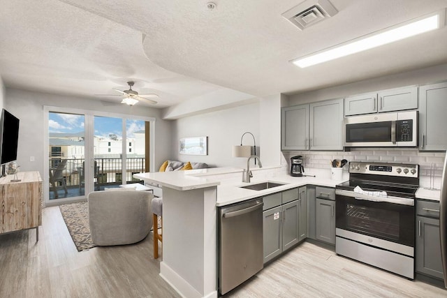 kitchen with light hardwood / wood-style floors, kitchen peninsula, stainless steel appliances, and gray cabinetry