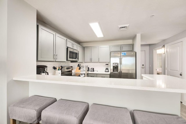 kitchen featuring tasteful backsplash, appliances with stainless steel finishes, kitchen peninsula, a kitchen breakfast bar, and gray cabinets