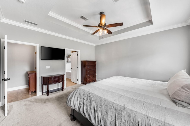 bedroom with a raised ceiling, light carpet, ensuite bathroom, and ceiling fan