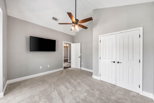 unfurnished bedroom featuring light colored carpet, a closet, high vaulted ceiling, and ceiling fan