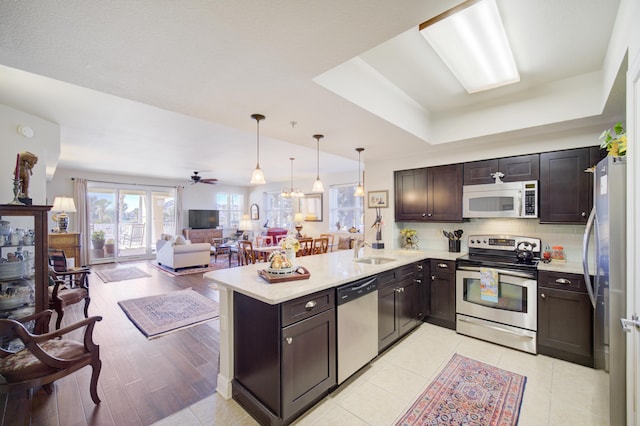 kitchen with kitchen peninsula, decorative backsplash, sink, light hardwood / wood-style floors, and stainless steel appliances