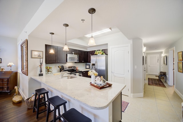 kitchen featuring hanging light fixtures, kitchen peninsula, a kitchen bar, light wood-type flooring, and appliances with stainless steel finishes