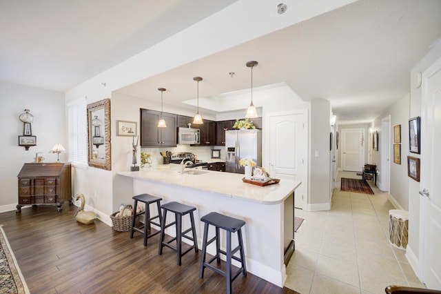 kitchen with kitchen peninsula, a breakfast bar area, light wood-type flooring, dark brown cabinetry, and stainless steel appliances