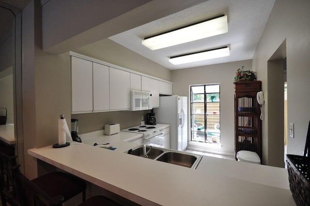 kitchen with white appliances, sink, kitchen peninsula, white cabinets, and a breakfast bar