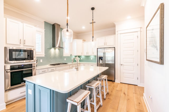 kitchen featuring built in appliances, wall chimney range hood, a kitchen island with sink, and light hardwood / wood-style floors