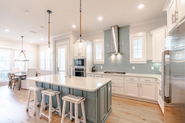 kitchen featuring white cabinetry, stainless steel appliances, wall chimney exhaust hood, and a kitchen island with sink