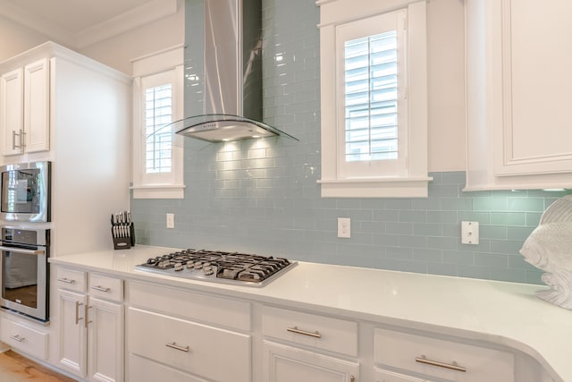 kitchen with wall chimney exhaust hood, white cabinets, stainless steel appliances, and plenty of natural light