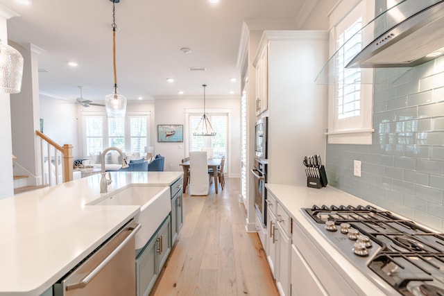 kitchen featuring wall chimney range hood, white cabinetry, light hardwood / wood-style floors, stainless steel appliances, and decorative backsplash