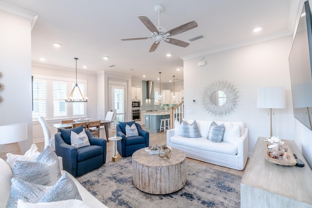 living room with light hardwood / wood-style flooring, ornamental molding, and ceiling fan with notable chandelier